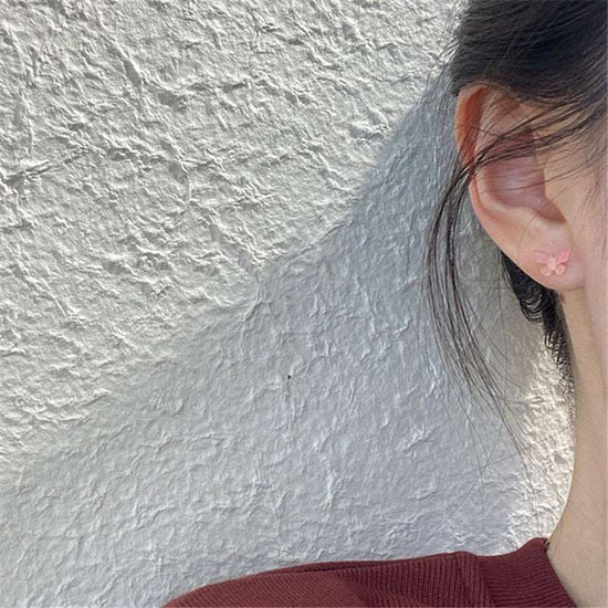 Dreamlit Butterfly Stud Earrings in Pink Orange styled on ear against a textured wall.