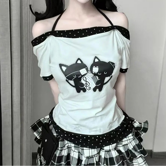 Front view of the model wearing the Bandaged Kitties Off-Shoulder Top featuring an adjustable halter strap, off-shoulder neckline, bandaged kitty graphic with musical note details, contrasting polka dot trim, and paw print and bone accents.