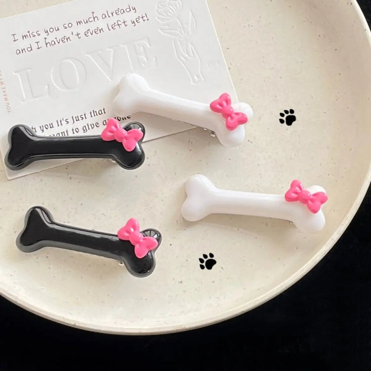 Flat lay of black and white Bowtiful Bones Hair Clips arranged on a plate, featuring glossy bone-shaped designs with pink bow accents.