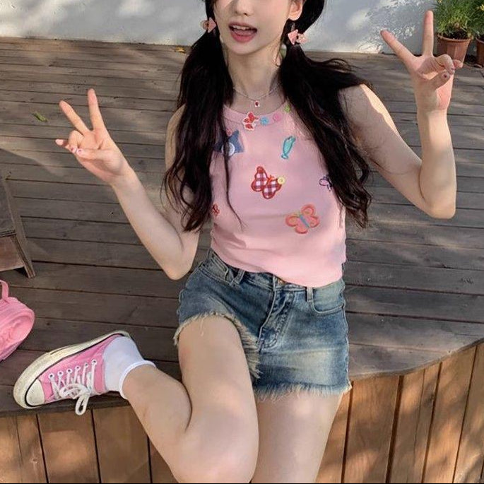 Full seated outfit view of a model wearing the dusty pink Charm Collector Tank, denim shorts, and pink sneakers.