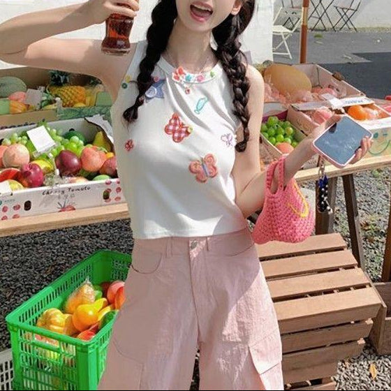 Standing model wearing the white Charm Collector Tank with pink pants beside market crates.