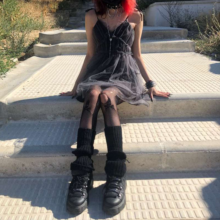 Model seated outdoors in Dark Fairy Tulle Dress, styled with black shoes, leg warmers, and a fishnet skull tights