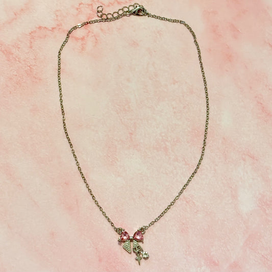 Flat lay of the Daydream Bow Necklace on pink marble background, highlighting bow charm