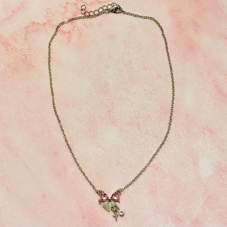 Flat lay of the Daydream Bow Necklace on pink marble background, highlighting bow charm