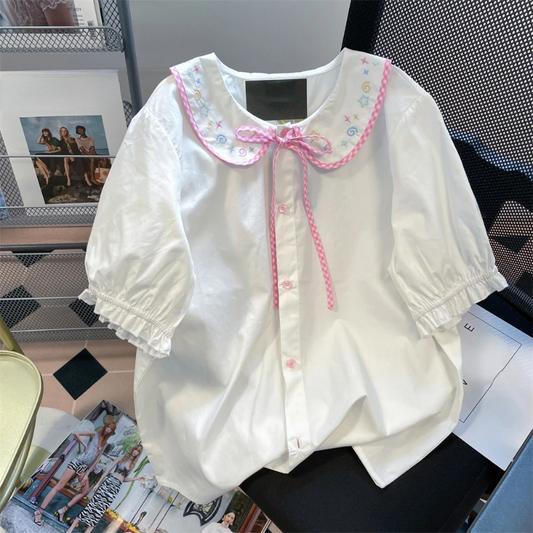 Front flat lay of the Doodle Darling Collar Blouse in white with pastel embroidered collar, pink gingham trim, and puff sleeves
