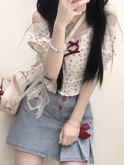 A front view of the Dual Darling Denim Skirt, focusing on the embroidered heart, pleated detail, and added sheer ribbon and red bow
