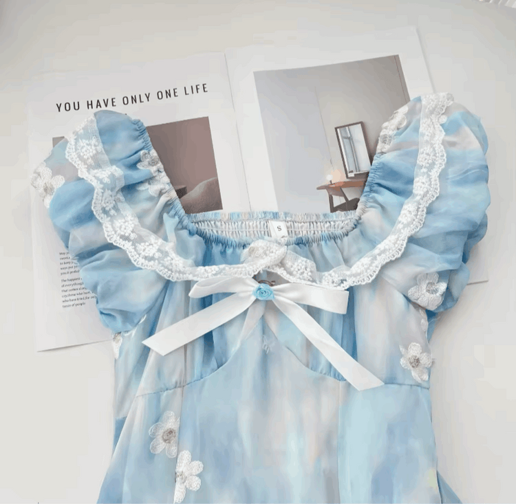 Detailed close-up of a flat lay of the mini Ethereal Flower Princess Dress, showcasing its lace trim, bow detailing, and floral embellishments.
