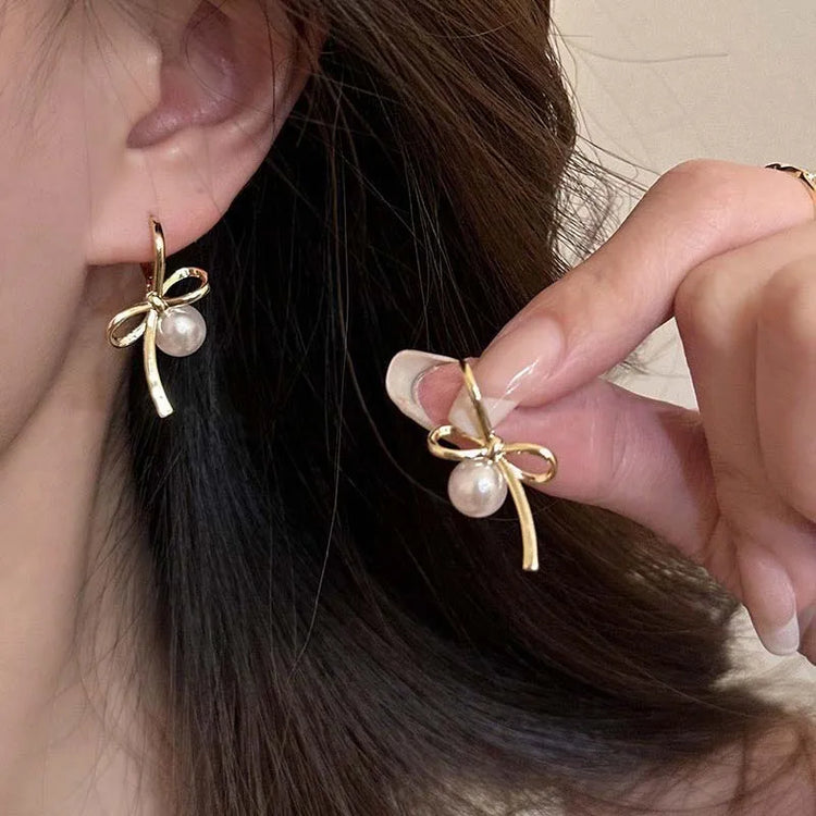 Model wearing and holding Gold Pearl Whim Bow Earrings close-up