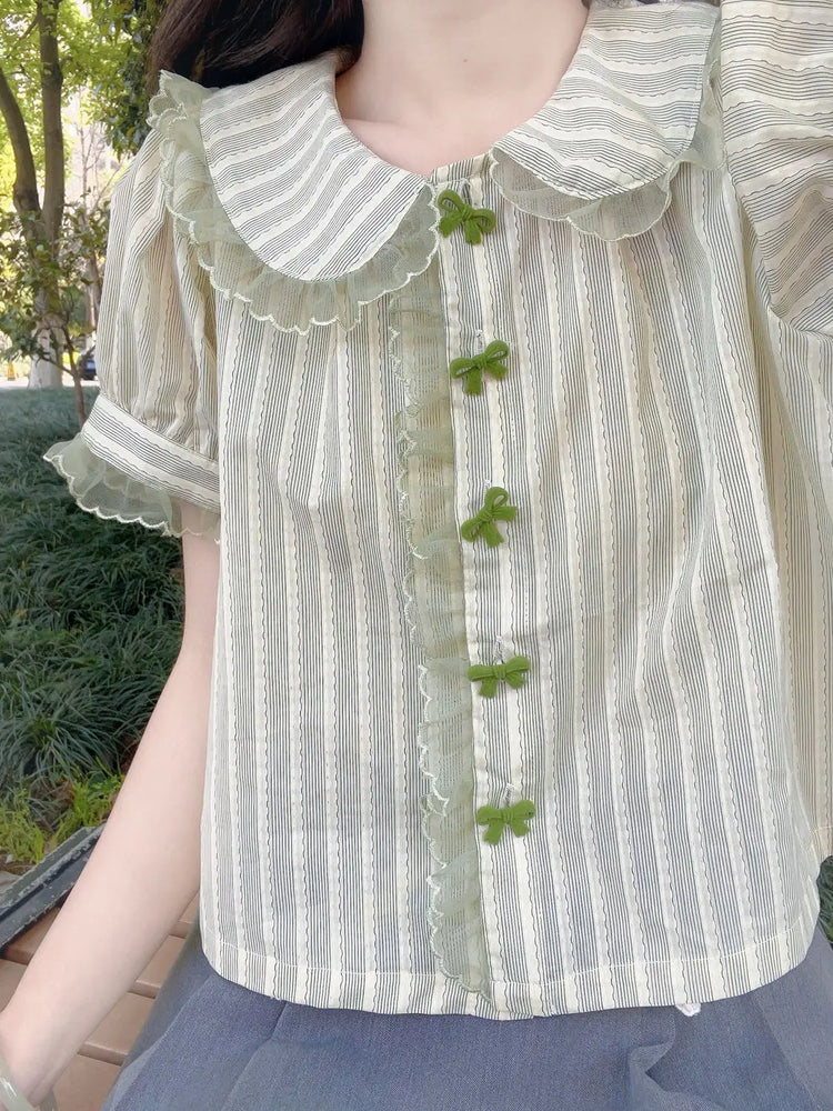 Model in a park wearing Pistachio Ribbon Striped Blouse with lace trim and bow buttons