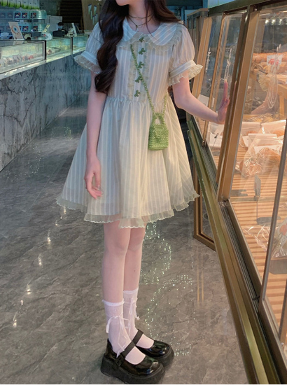 Model in the mini-length Pistachio Ribbon Striped Dress, styled with ribbon socks and black platforms, standing beside a glass bakery display.