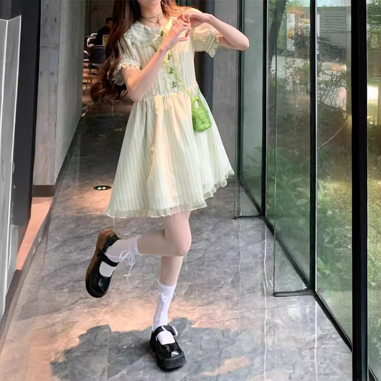 Model in mini Pistachio Ribbon Striped Dress making a heart sign with her hands in a bright hallway.