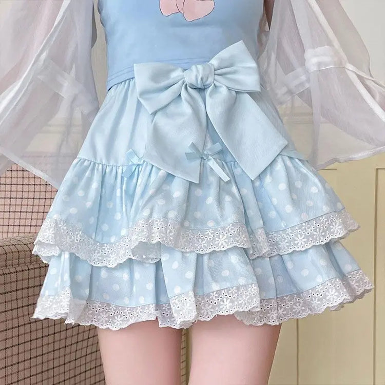 Model wearing the Polka Dot Sweetie Tiered Skirt in blue with lace ruffles, layered tiers, ribbon accents, and a removable oversized bow pin.