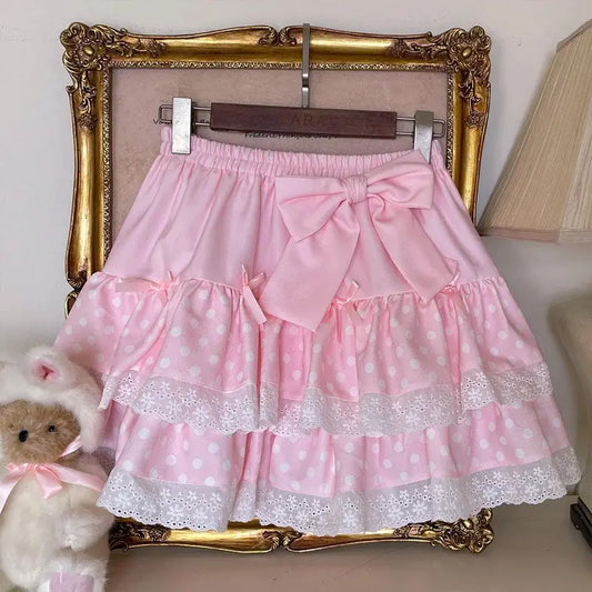 The Polka Dot Sweetie Tiered Skirt in pink displayed on a hanger with tiered lace trim, polka dot ruffles, and a removable oversized bow pin.