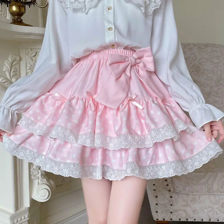 Model wearing the Polka Dot Sweetie Tiered Skirt in pink with layered lace ruffles, polka dot fabric, ribbon accents, and a removable oversized bow pin.