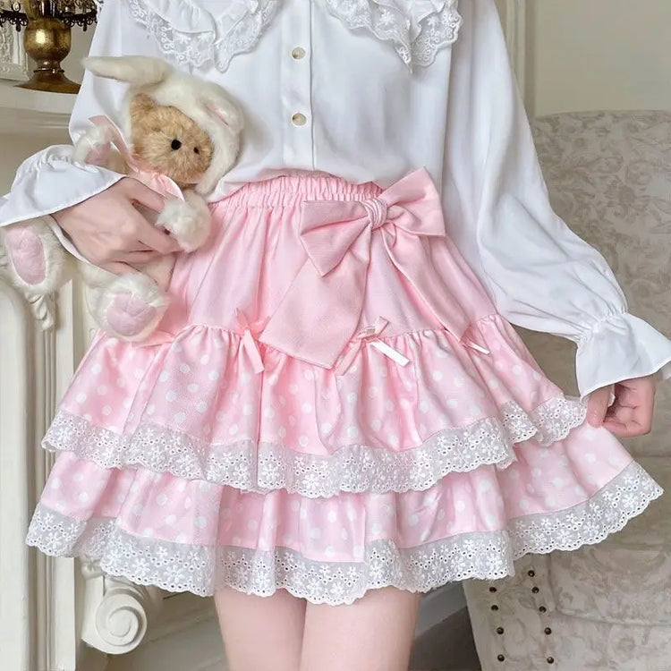 Close-up of the Polka Dot Sweetie Tiered Skirt in pink featuring lace trim, layered polka dot ruffles, ribbon bow accents, and a removable oversized bow pin.