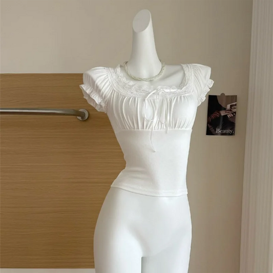 White Ruffled Romance Top displayed on a mannequin with a lace-trimmed square neckline, ribbon ties, gathered bust, and ruffled puff sleeves.