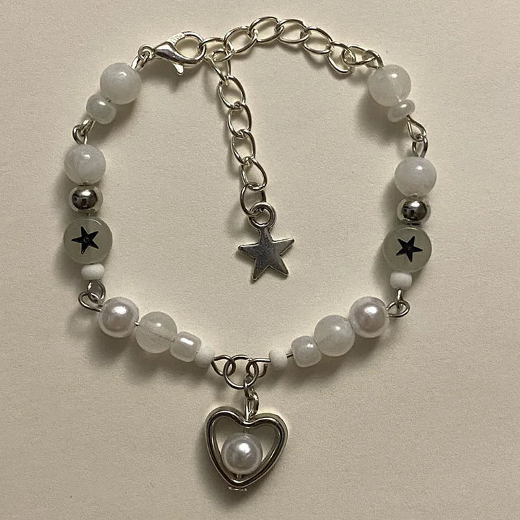 Close-up of the white Set Apart Star Bracelet with pearl heart charm and black star beads on a light background.