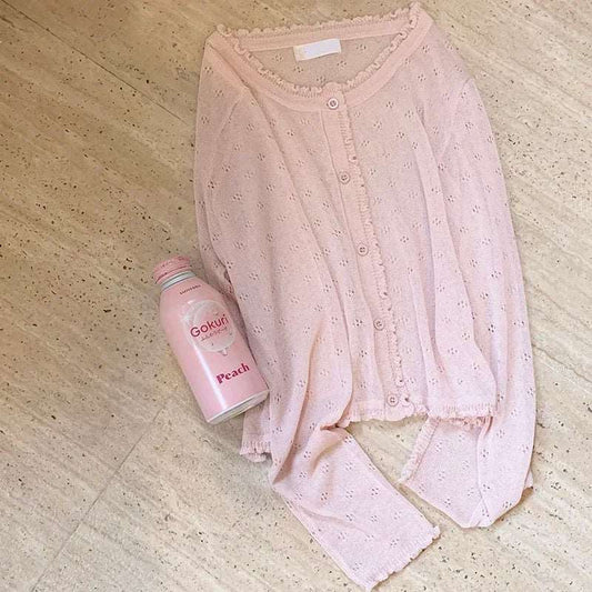 Flat lay of blush pink Sheer Sweetness Cardigan beside a pastel peach drink