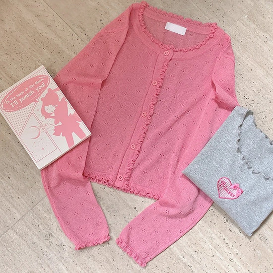 Hot pink Sheer Sweetness Cardigan flat laid next to folded tee and manga