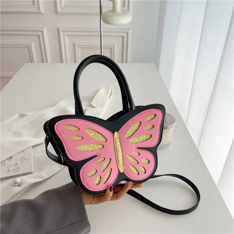 Sparkling Butterfly Handbag in black and pink being held from the bottom on a table by a model