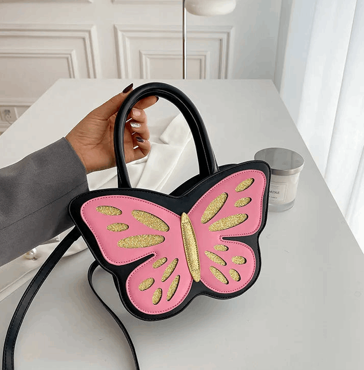 Sparkling Butterfly Handbag in black and pink being held by the handle on a table by a model