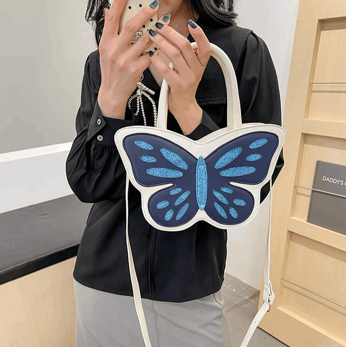 Model holding Sparkling Butterfly Handbag in white and blue in front of their body in a mirror