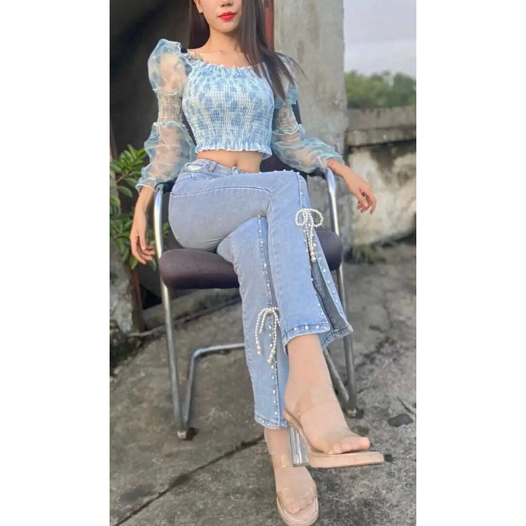 Model sitting with legs crossed wearing the Split Statement Pearl Jeans with calf-high slits and pearl bow details