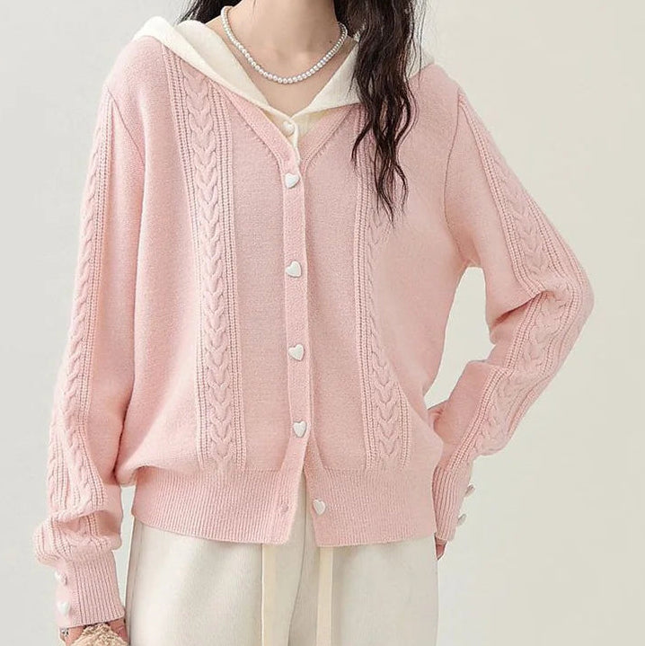 Model wearing the Sweetheart Cable Knit Cardigan in light pink with cream hood, showing the heart-shaped buttons and cable knit detailing.