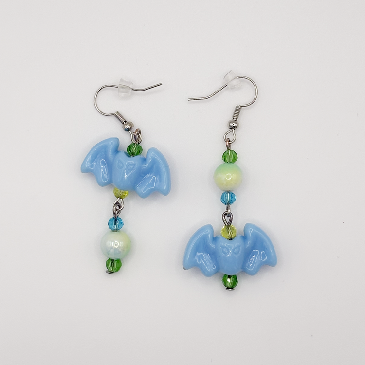 Two Moody Originals Candy Bite Bat Earrings with pastel blue bat charms and green, blue, and yellow glass and acrylic beads in playful opposite designs.