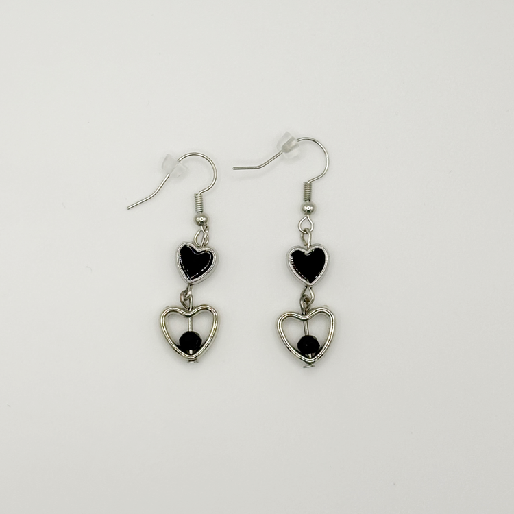 Two Moody Originals: Lovesick Charm Earrings with glossy black heart charms, silver open heart drops, and black crystal bead accents.
