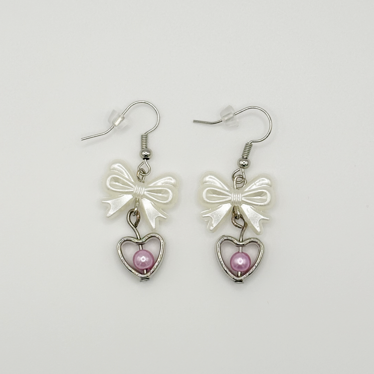 Two Moody Originals: Softhearted Bow Earrings with white bow charms, silver heart pendants, and pink faux pearl accents on silver hooks.