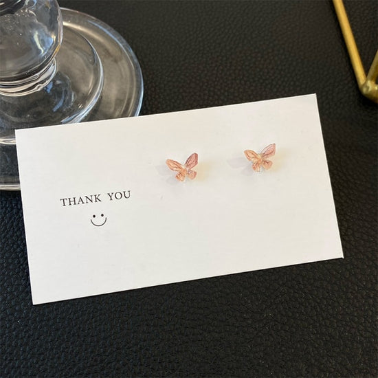 Dreamlit Butterfly Stud Earrings in a delicate peachy pink hue resting against a white card.