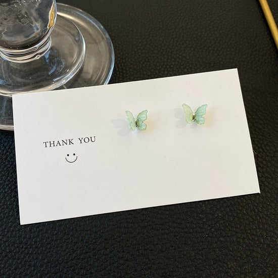 A pair of Dreamlit Butterfly Stud Earrings in sea green displayed on a minimal thank-you card.