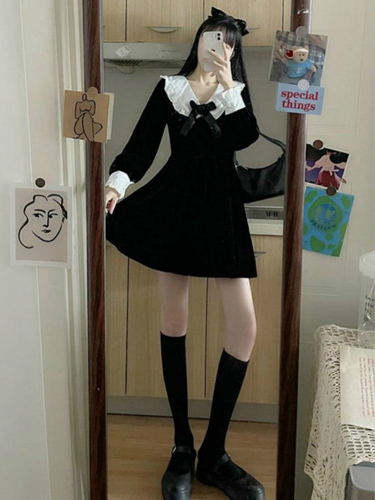 Front view of model wearing Midnight Sailor Mini Dress with long sleeves and sailor collar in black while holding the end of the dress