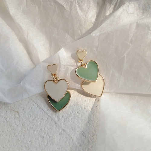 Flat-lay of Olive You Triple Heart Earrings on crumpled white paper, showing stacked olive green and ivory hearts with gold-tone edges.