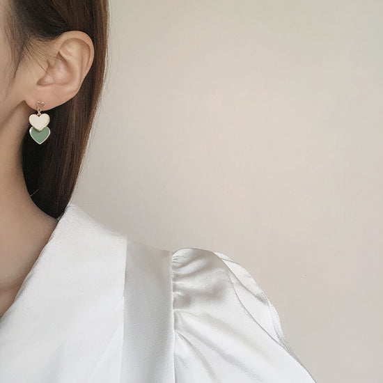 Close-up of a model wearing Olive You Triple Heart Earrings, featuring three stacked hearts in olive green and ivory hanging from gold-tone hooks