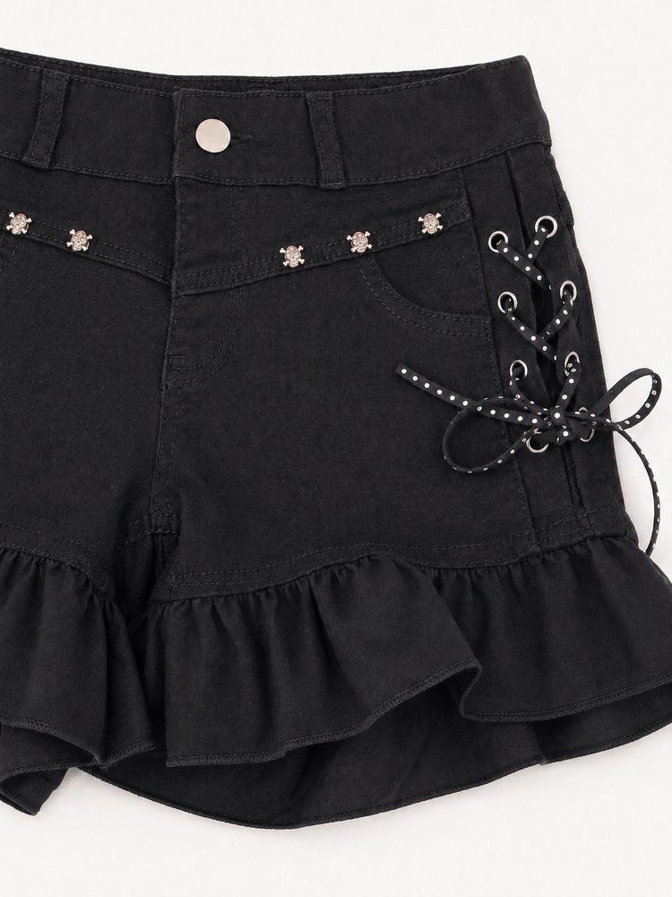 Close-up of Two Moody Originals: Pretty Dangerous Shorts showing skull embellishments, studded ribbon lacing, and ruffle trim details.