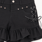 Close-up of Two Moody Originals: Pretty Dangerous Shorts showing skull embellishments, studded ribbon lacing, and ruffle trim details.