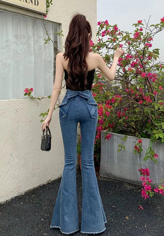 Model standing in front of flowers, showing the back view of the Dark Blue Backstage Bow Flare Jeans, showcasing the bow detail.