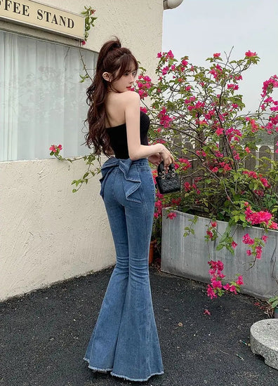Mode posing and showing the back view of the Dark Blue Backstage Bow Flare Jeans.