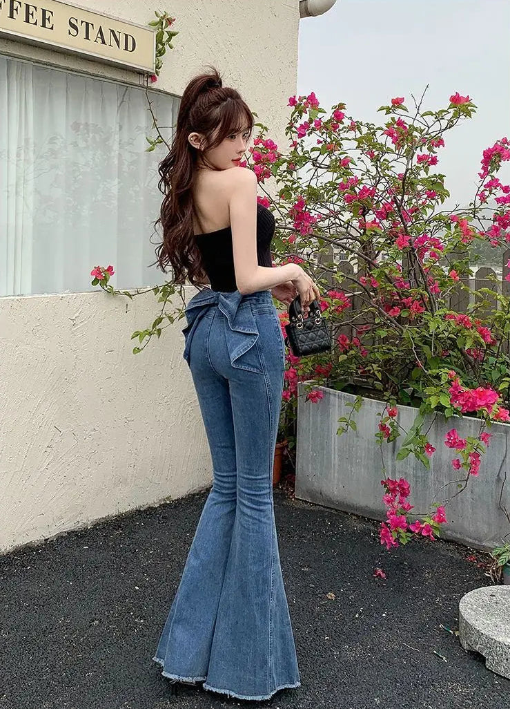 Mode posing and showing the back view of the Dark Blue Backstage Bow Flare Jeans.