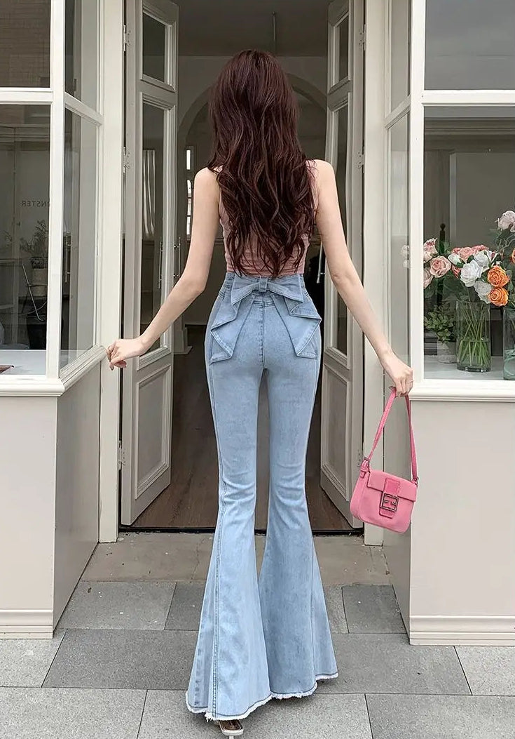 Model standing in a doorway showing the back view of the Light Blue Backstage Bow Flare Jeans highlighting the bow accent.