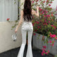 Model standing in front of flowers in the white Backstage Bow Flare Jeans, showcasing the bow detail in the back.