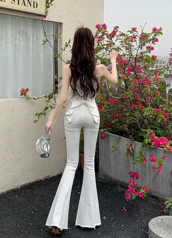 Model standing in front of flowers in the white Backstage Bow Flare Jeans, showcasing the bow detail in the back.