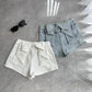 Flat lay of the Backstage Bow Shorts in white and light blue.