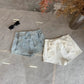 Overhead flat lay of the Backstage Bow Shorts in white and light blue.