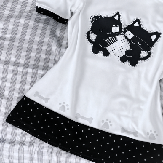 Close-up view of the Bandaged Kitties Off-Shoulder Top, highlighting the bandaged kitty graphic, contrasting polka dot trim, and decorative paw print and bone accents along the hem.