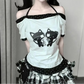 Front view of the model wearing the Bandaged Kitties Off-Shoulder Top featuring an adjustable halter strap, off-shoulder neckline, bandaged kitty graphic with musical note details, contrasting polka dot trim, and paw print and bone accents.