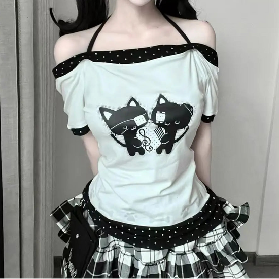 Front view of the model wearing the Bandaged Kitties Off-Shoulder Top featuring an adjustable halter strap, off-shoulder neckline, bandaged kitty graphic with musical note details, contrasting polka dot trim, and paw print and bone accents.