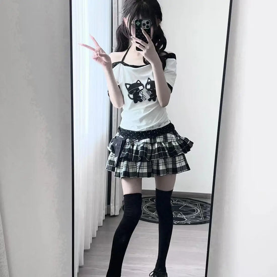 Full outfit view of the model wearing the Bandaged Kitties Off-Shoulder Top styled with a layered plaid skirt and thigh-high socks.